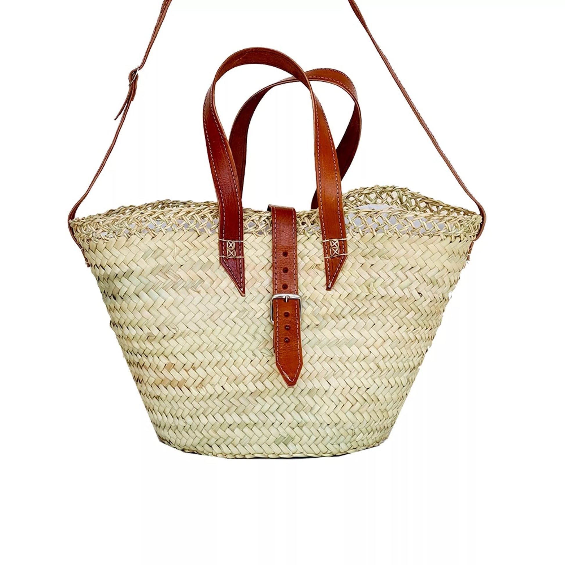 A tote basket made of palm fiber, featuring a caramel leather handle and shoulder strap, with a pouch closure and zip pocket.